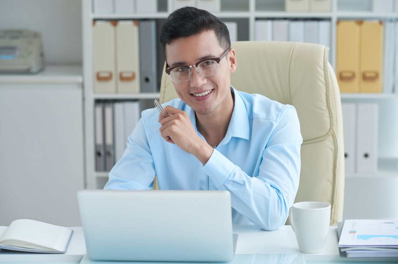 uomo sorridente con occhiali seduto dietro a una scrivania in ufficio
