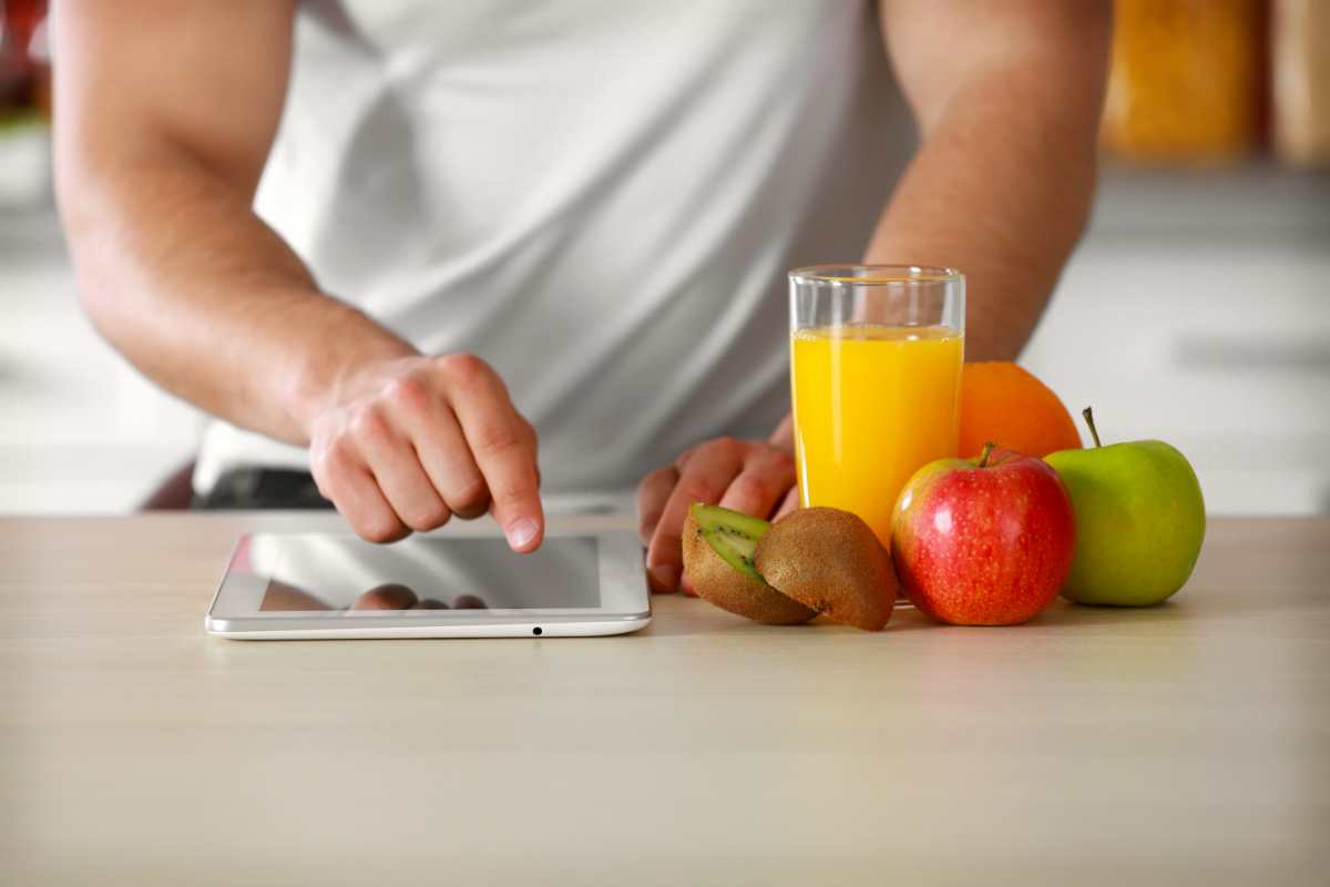uomo controlla sul tablet le calorie della frutta di stagione che ha davanti a sé sul tavolo